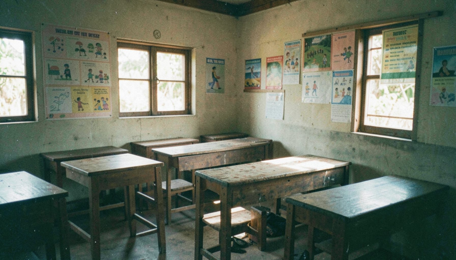 A softly lit classroom scene in rural Ghana with wooden desks and colorful learning posters on the walls, warm natural light falling across the room