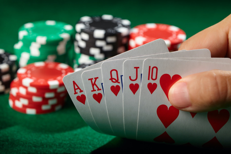 Close-up of a hand holding a royal flush playing card hand with poker chips in red, green, and black in the background
